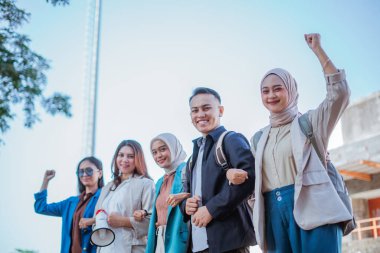 Mutlu öğrenciler el ele tutuşup yumruk sallıyorlar.