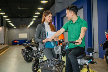Satıcı kadın, satın almadan önce elektrikli bisiklet ürünü deneyen erkek müşterilere hizmet veriyor.