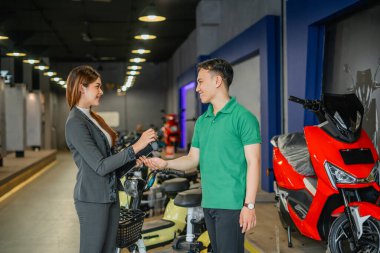 Erkek müşteri satıcı kadından elektrikli bisiklet anahtarı alıyor