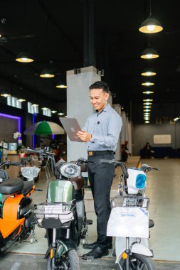 Asyalı işçilerin galeride tablet kullanarak elektrikli bisikleti kontrol etmesi.