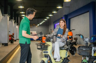 Erkek çalışan, galeride bayan müşteriye yeni elektrikli bisiklet teklif ediyor.