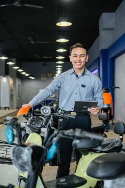 Asyalı yönetici elinde tablet tutuyor. Elektrikli bisiklet dükkanında çalışıyor.