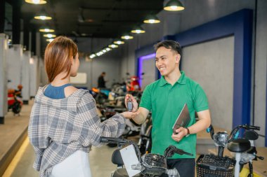 Satıcı bayan müşteriye yeni elektrikli bisiklet anahtarı veriyor.