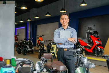 Asyalı elektrikli bisiklet satıcısı elinde gülen yüzlü tablet tutuyor.