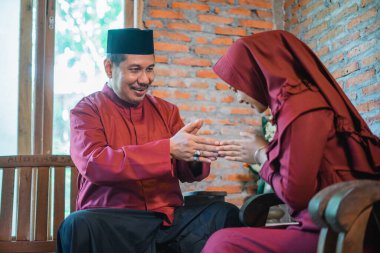 Asyalı Müslüman koca, karısına evde mutlu bayramlar dilemek için el hareketi yapıyor.