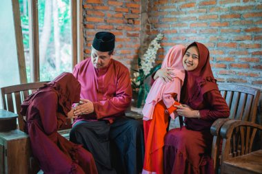 Anne ve baba evde bayram kutlaması sırasında el sıkışıyor ve iki küçük kızına sarılıyorlar.