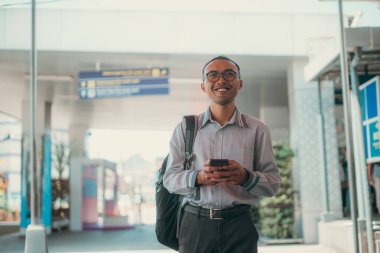 Neşeli bir gezgin havaalanı terminalinde beklerken mutlu bir şekilde akıllı telefon kullanıyor.