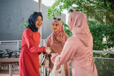 Havalı tesettürlü üç neşeli kadın açık havada keyifli bir anı paylaşıyor.