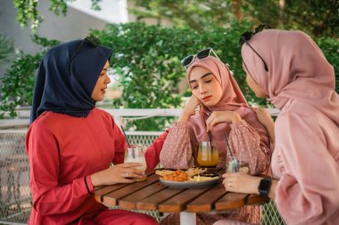 Üç arkadaş abur cubur ve içecekleri paylaşır, güneşli bir kafede kaliteli zaman geçirirler.