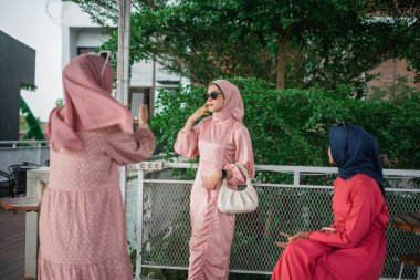 Üç şık giyinmiş kadın güzel bir açık hava ortamında sosyal bir toplantının tadını çıkarıyorlar.