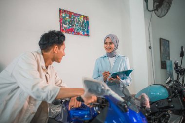 Yakışıklı adam gündelik giysiler giyip galeride peçeli satıcı kadınla motosikletlere bakıyor.