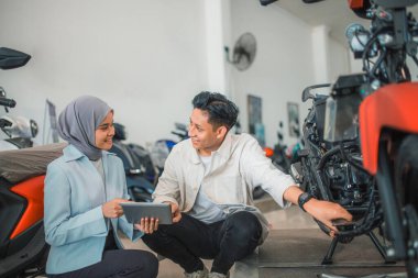 Yakışıklı Asyalı adam, galeride tabletli bir satıcıyla yeni motosikletini kontrol ediyor.