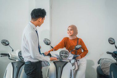 Bir bayan müşteri motosiklet galerisinde erkek bir satıcıyla yeni bir motosiklet deniyor.