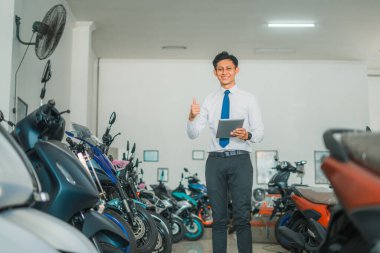 Kravatlı adam arka planda motosiklet galerisi olan bir tablet kullanırken başparmak gösteriyor.