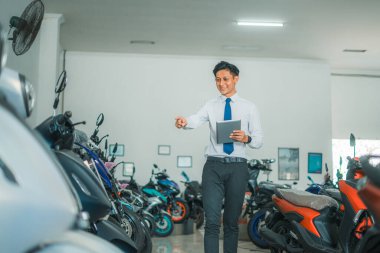 Satış müdürü, galeride kontrol sırasında motosikletlerden birini işaret ederken bir tablet taşıyor.