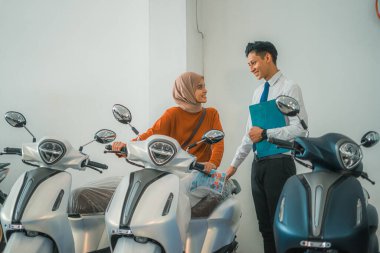 Müslüman kadın ziyaretçi sohbet eder ve motosiklet galerisinde erkek bir satıcıyla yeni bir motosiklet dener.