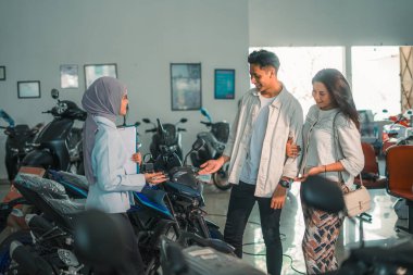 Karı koca, bir araba fuarında satıcı bir kadınla yeni bir motosiklet deniyorlar.