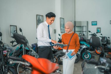 Motosikletli satıcı, motosiklet galerisinde peçeli bir kadın ziyaretçiyle sohbet ediyor.