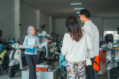 Satıcı kadın duvak takıp gülümsüyor ve çiftleri galeriye davet ediyor.