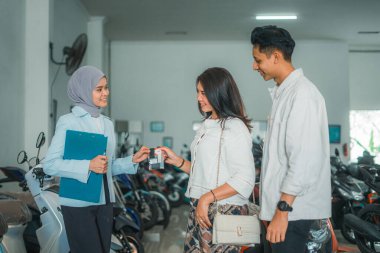 Peçeli bayan garson galerideki birkaç müşteriye yeni bir motosiklet mülkiyeti tabelası veriyor.