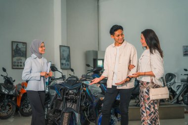 Motosiklet dükkanından almadan önce yeni motosikletlere bakan genç bir çift.