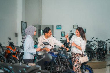 Başparmakları havada bir kadın galeride yeni motosikletinin üzerinde oturan erkek ortağını över.