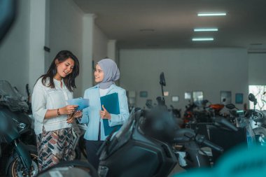 Motosiklet galerisinde peçeli bir satıcıyla sohbet eden genç bir kadın.
