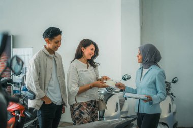Asyalı kadın ve erkek, galeride tesettürlü bir satıcıdan satın alma belgesi alıyorlar.
