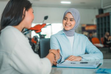 Bir kadın tezgahtar motosiklet galerisinde müşteriyle tokalaşıyor.