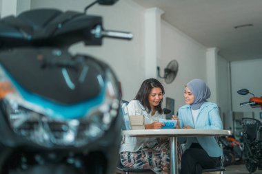 Bir kadın ziyaretçinin seçici odağı ve galeride oturmuş sohbet eden bir satıcı.