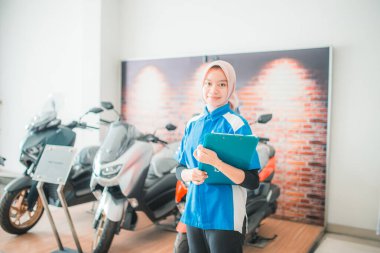 Üniformalı kadın, sergide yeni bir motosikletin arka planına karşı bir pano tutuyor.