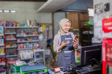 Neşeli bir bayan işçi markette akıllı telefonunu kullanmaktan mutluluk duyar.