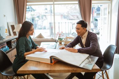 Perde dükkanındaki katalog kitabından pencere tedavisini seçen Asyalı müşteriye yardım eden güzel bir esnaf.