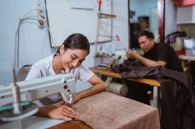 Perde yapımı için kumaşı diken Asyalı kadın terzi. Prodüksiyon binasının arka planında çalışan erkek terzi.