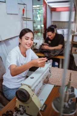 Güzel bir terzi, dikiş makinesine iplik yerleştirirken, aynı zamanda pencere bakımı yapım evinde çalışıyor.