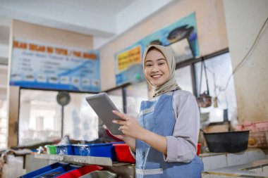 Önlüklü neşeli bir kadın çalışma alanında bir tabletle karşılaşır ve kendini işine adadığını gösterir.