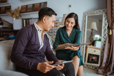 Kadın esnaf kataloğa bakarken erkek müşteriye pencere tedavisini seçmesinde yardımcı oluyor.