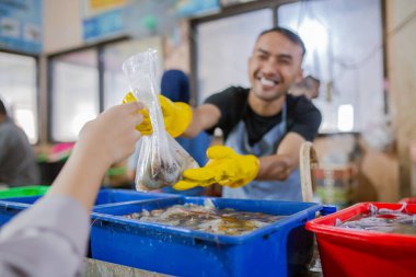 Neşeli bir satıcı kalabalık bir markette müşteriye taze deniz ürünleri veriyor..
