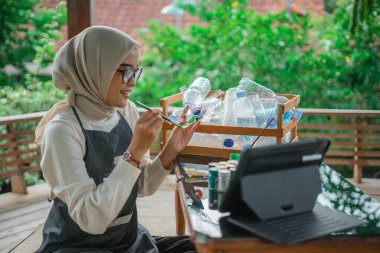 Geri dönüştürülmüş plastik şişe zanaatı yapan ve boyayan tesettürlü kadın.