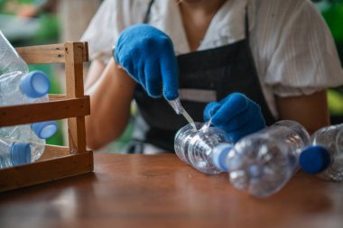 Ekin görünümlü önlük ve eldiven giyen kadın plastik şişeden el yapımı zanaat yapıyor.