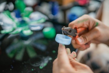 Kadın elini şişe kapağı atıklarından araç gereçler kullanarak kapat