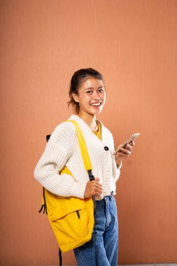 Parlak sarı bir sırt çantası olan ve akıllı telefonunu kullanan çok mutlu bir genç kadın.
