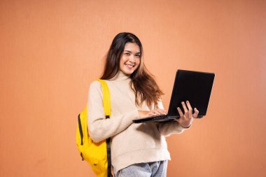 Genç bir öğrenci, yaratıcı ve modern bir ortamda dizüstü bilgisayar ve sarı sırt çantasıyla meşgul oluyor.