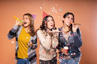 Konfeti, parti şapkası ve neşeli ifadelerle kutlama yapan üç arkadaş.