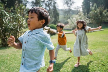 Çocuklar neşeyle koşuyor ve birlikte gülüyorlar hayat dolu canlı bir açık hava ortamında.