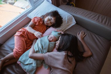 Yeni doğmuş güzel bir bebeğe bakan iki sevgili kız kardeşin yer aldığı sıcak bir aile sahnesi.