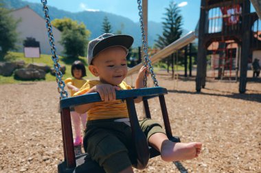 Mutlu bir çocuk, doğa ve eğlence aktiviteleriyle çevrili güzel bir parkta neşeyle sallanır.
