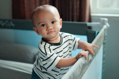 Oyunbaz ve meraklı bir bebek, şirinliklerini ve masumiyetlerini sergileyerek beşiğin üzerine eğilir.