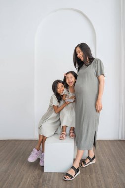 Hamile bir kadın zarif bir şekilde iki küçük kızın yanında duruyor. Kendisiyle birlikte anın tadını çıkarıyor gibi görünüyorlar.