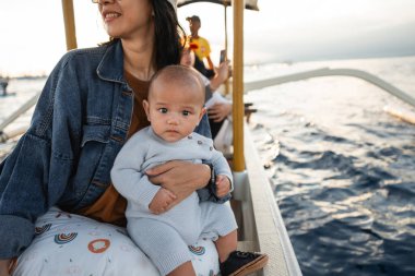 Bir kadın, geniş okyanus dalgalarında yüzen bir teknede huzur içinde küçük bir bebeği nazikçe tutuyor.